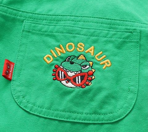 Green fabric with a dinosaur embroidered design and a red tag on a light blue background.