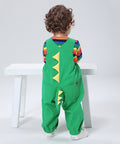 Child wearing a green dinosaur-themed outfit with a rainbow striped shirt, sitting on a white stool against a light gray background.