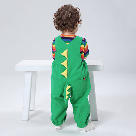 Child wearing a green dinosaur-themed outfit with a rainbow striped shirt, sitting on a white stool against a light gray background.
