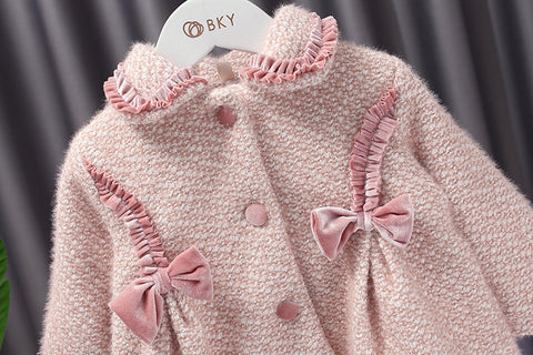 Pink children's coat with decorative bows on a hanger against a dark background
