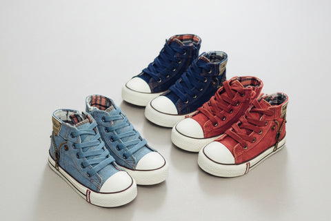 Two pairs of children's high-top sneakers, one blue and one red, on a light wooden surface.