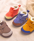 Four colorful children's boots on a soft surface with a hand holding one boot.