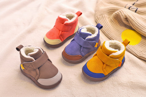 Four colorful children's boots on a soft surface with a hand holding one boot.