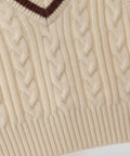Close-up of a beige sweater with a hand holding it, on a light background