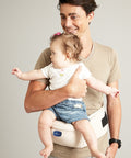 Man holding a baby in a white baby carrier against a plain background
