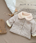 Children's checkered coat with fluffy collar and matching beanie on a textured surface.