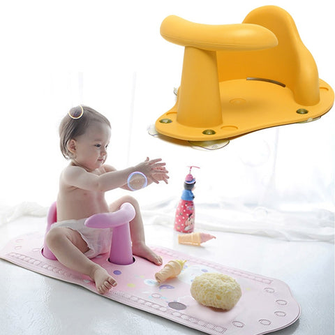 Baby sitting on a pink bath seat with a yellow bathtub support, playing with toys on a white mat.