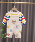 Children's outfit with striped shirt and bear-themed overalls on a hanger against a gray curtain background.