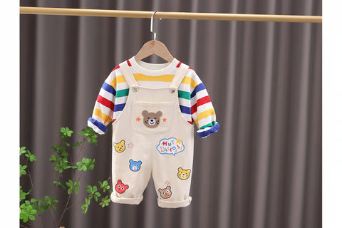 Children's outfit with striped shirt and bear-themed overalls on a hanger against a gray curtain background.