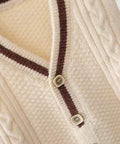 Close-up of a cream-colored cable knit cardigan with brown buttons on a white background