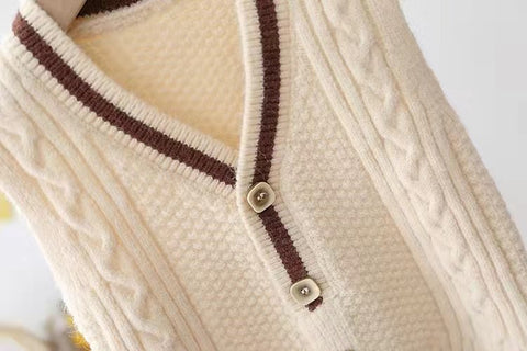 Close-up of a cream-colored cable knit cardigan with brown buttons on a white background