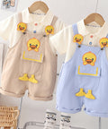 Children's clothing set with beige and blue overalls and matching shirts on hangers against a white wall.