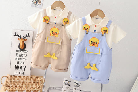 Children's clothing set with beige and blue overalls and matching shirts on hangers against a white wall.