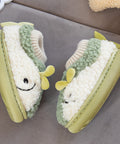 Pair of green and white baby shoes with smiling faces on a gray surface