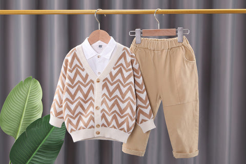 Children's clothing set with chevron cardigan and beige pants on hangers against a gray curtain background.