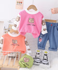Children's clothing set with pink and orange tops and blue pants on hangers against a white tiled wall.