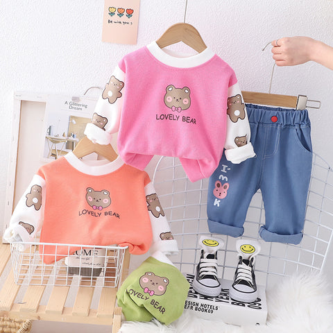 Children's clothing set with pink and orange tops and blue pants on hangers against a white tiled wall.