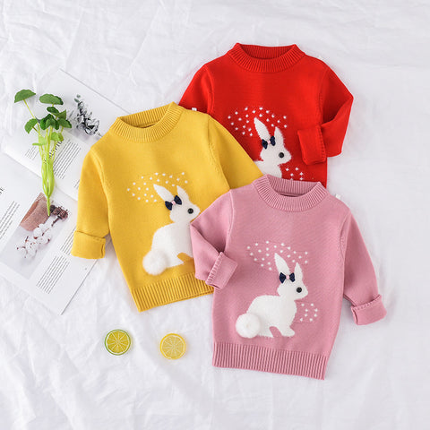 Three children's sweaters in red, yellow, and pink with rabbit designs on a white background.