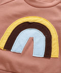 Close-up of a pink garment with a rainbow patch featuring yellow, brown, and blue colors.