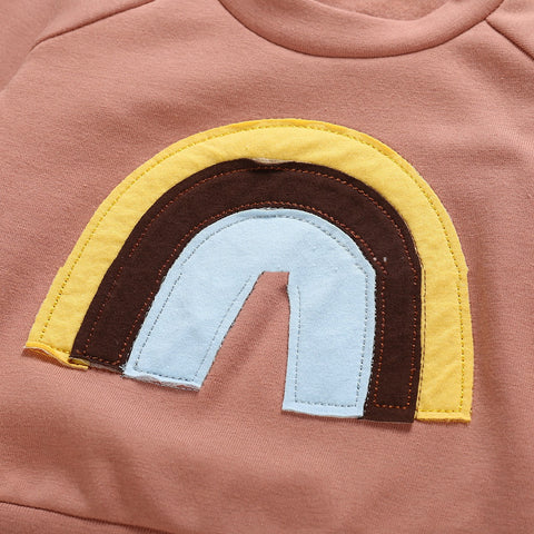 Close-up of a pink garment with a rainbow patch featuring yellow, brown, and blue colors.