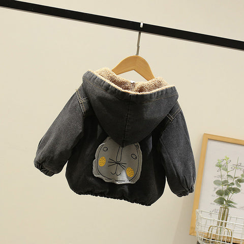 Children's denim jacket with a hood and bear face patch on a hanger against a beige wall.