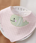 Pink baby bib with green whale design on a white surface