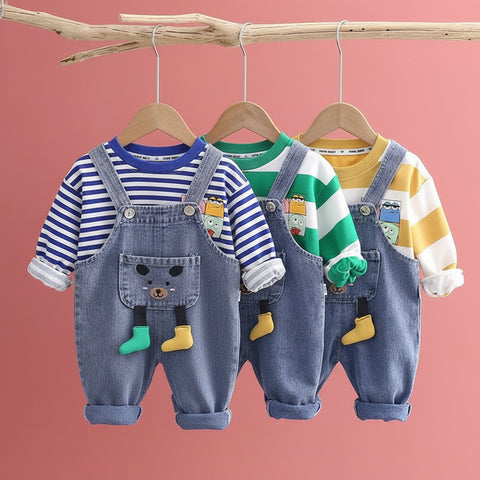 Three children's outfits with denim overalls and colorful shirts on hangers against a light gray background.