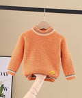 Orange sweater on a hanger against a beige wall with a plant and framed picture in the background.