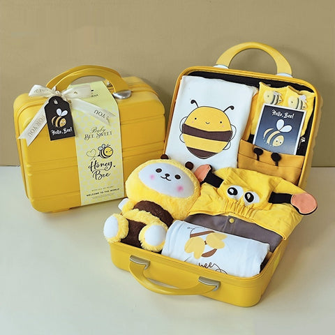 Yellow baby gift set with bee-themed items in an open suitcase on a beige background