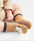 Baby wearing brown socks with bear design and beige outfit on a light background