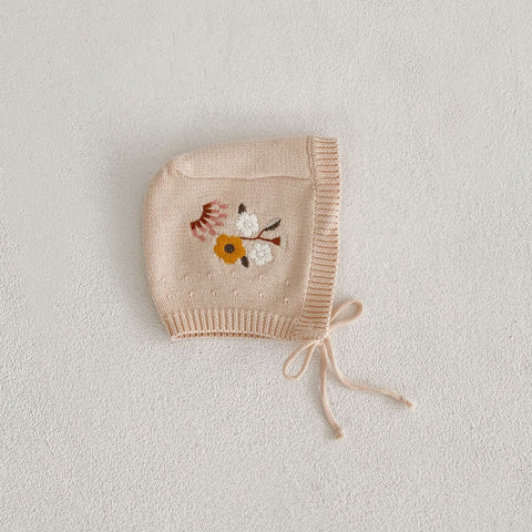 Knitted baby bonnet with floral embroidery on a light gray background