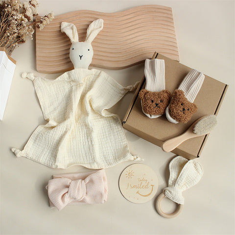 Collection of baby items including a plush toy, socks, a headband, and a wooden brush on a neutral background.