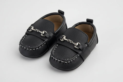 Pair of black leather shoes with silver buckles on a light gray background