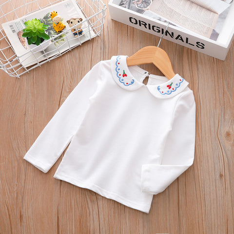 White long-sleeve shirt with embroidered collar on a wooden surface