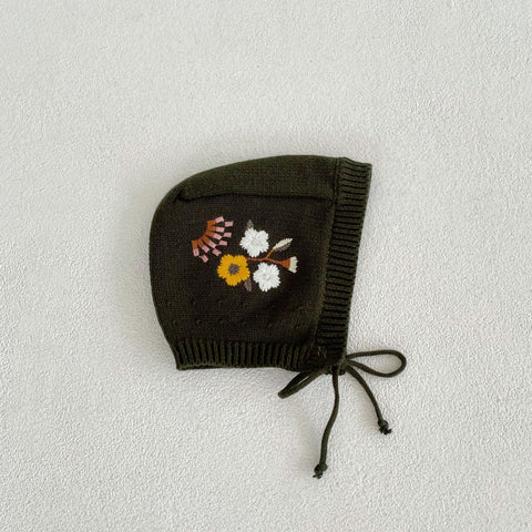 Dark green knitted baby bonnet with floral embroidery on a light gray background