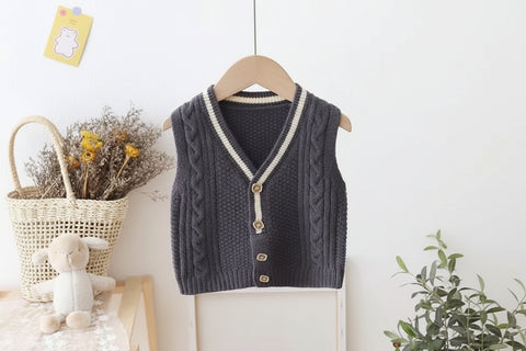 Dark gray knitted vest with white trim on a hanger against a light background