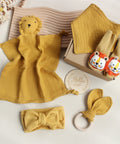 Yellow baby comfort blanket, booties, headband, and teething ring on a light background