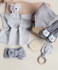 Collection of baby items including a soft toy, socks, headband, and teether on a neutral background.