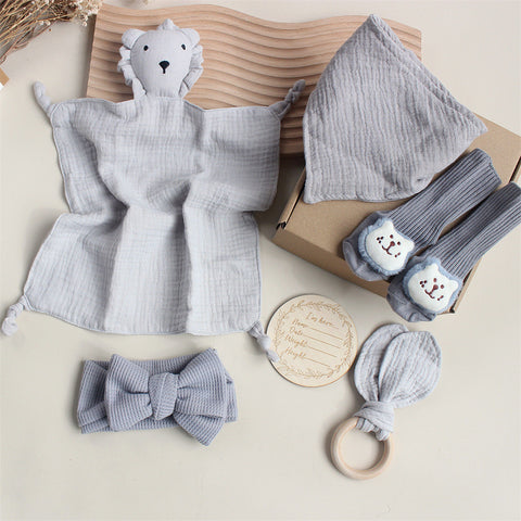 Collection of baby items including a soft toy, socks, headband, and teether on a neutral background.