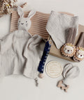 Collection of baby items including a plush bunny, blanket, and toys on a light surface.
