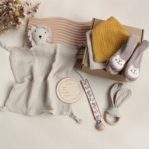 Collection of baby items including a plush toy, blanket, and rattle on a neutral background