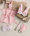 Collection of pink baby items including a blanket, socks, headbands, and a teether on a neutral background.