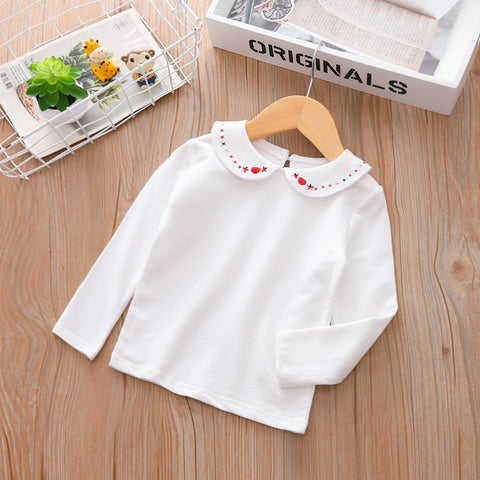 White long-sleeve shirt with embroidered collar on a wooden surface