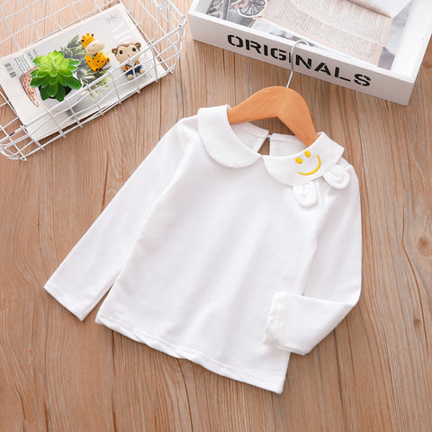 White children's shirt with a smiley face design on a wooden surface