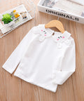 White children's blouse with a decorative collar on a wooden surface