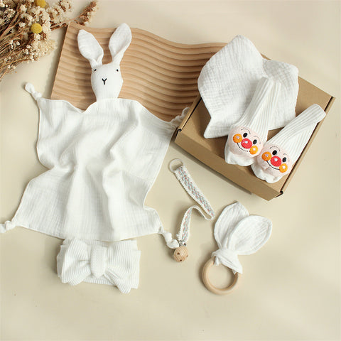 Baby comfort items including a white rabbit plush toy, socks with cartoon characters, and a teething ring on a beige surface.