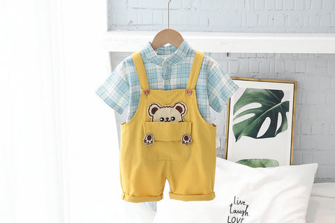 Yellow romper with bear design and plaid shirt on hanger against a light gray wall.