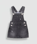 Black denim pinafore dress with white buttons on a white background