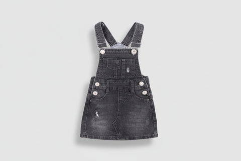 Black denim pinafore dress with white buttons on a white background