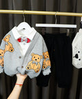 Children's clothing with teddy bear pattern on a hanger against a dark curtain background